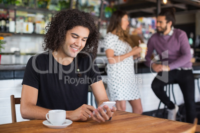 Smiling young man using mobile phone while sitting in restaurant