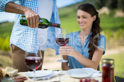 Man pouring red wine in glass held by woman