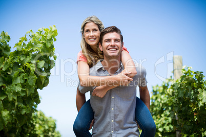 Young couple piggybacking at vineyard against blue sky