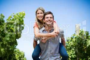 Young couple piggybacking at vineyard against blue sky