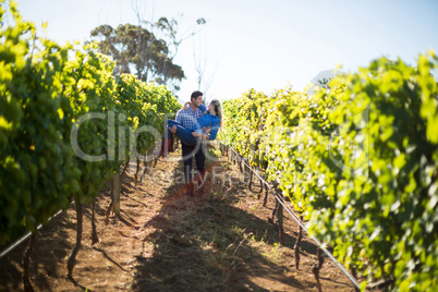 Man carrying his girlfriend amidst plants at vineyard