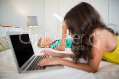 Siblings using digital tablet and laptop on bed