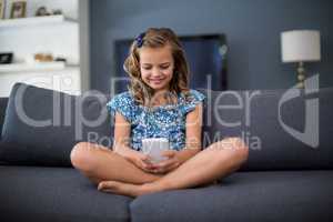 Happy girl sitting on sofa and using mobile phone in living room