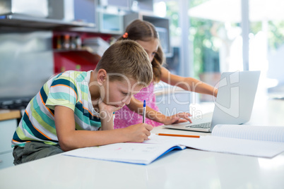 Boy doing his homework while girl using laptop in kitchen