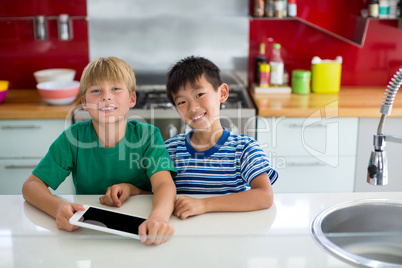 Portrait of smiling siblings using digital tablet in kitchen