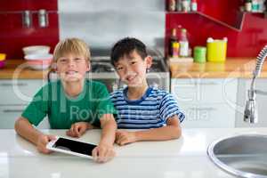 Portrait of smiling siblings using digital tablet in kitchen