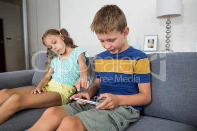 Smiling siblings using digital tablet on sofa in living room Smiling siblings using digital tablet on sofa in living room