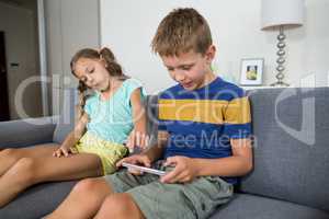 Smiling siblings using digital tablet on sofa in living room