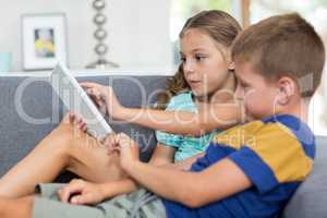 Siblings using digital tablet in living room