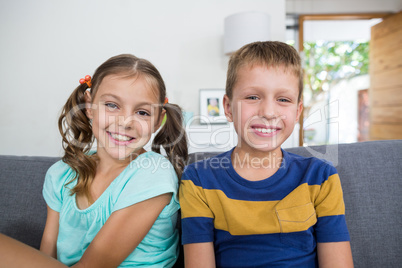 Smiling siblings sitting together on sofa in living room