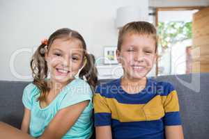 Smiling siblings sitting together on sofa in living room