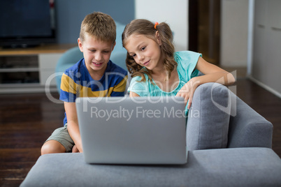 Smiling siblings using laptop in living room