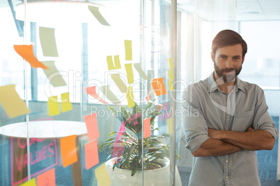 Portrait of confident businessman with arms crossed standing by strategy on glass at office