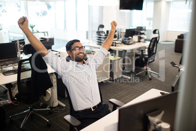Happy businessman with arms raised in office