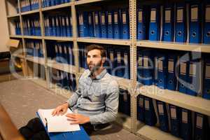 Businessman with file sitting on floor in storage room