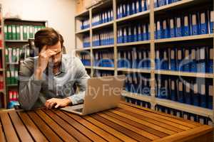 Tensed business executive using laptop in file storage room