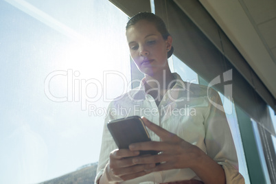 Businesswoman using mobile phone in office on sunny day