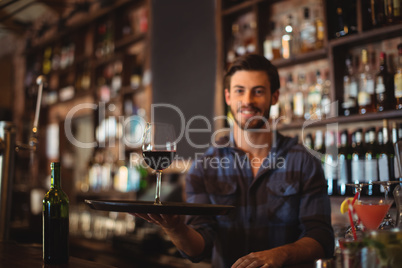 Portrait of bar tender holding a tray with glass of red wine