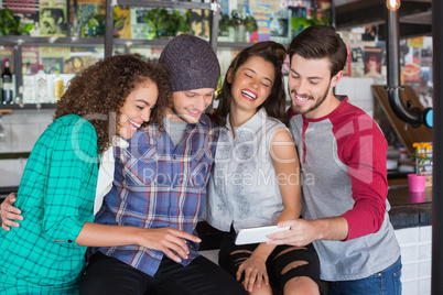 Cheerful friends laughing while watching mobile phone in restaurant