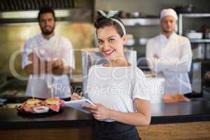 Waitress writing while chef standing in kitchen