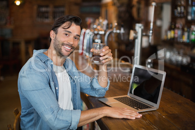 Young man holding beer while sitting by laptop in pub