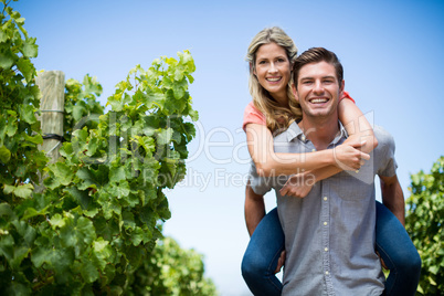 Happy couple piggybacking at vineyard against blue sky