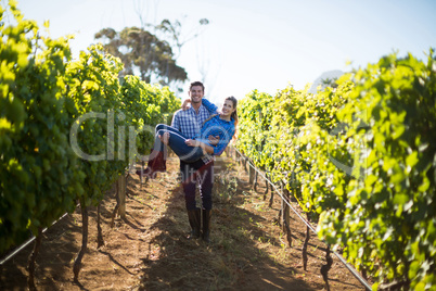 Portrait of man carrying his girlfriend amidst plants at vineyard