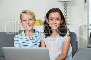 Smiling siblings sitting on sofa with laptop in living room