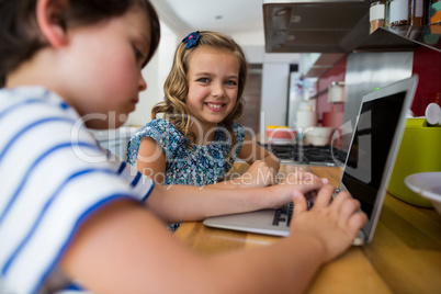 Smiling siblings using laptop in kitchen