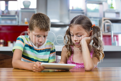 Siblings using digital tablet in kitchen