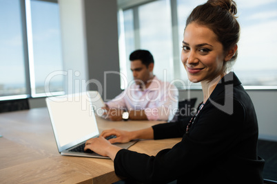Businesswoman typing on laptop at table with male colleague in background