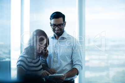 Smiling business couple using digital tablet against glass window
