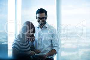 Smiling business couple using digital tablet against glass window