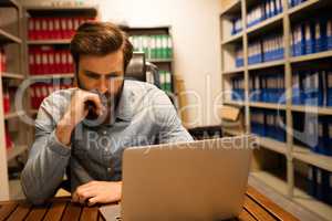 Thoughtful business executive using laptop in file storage room