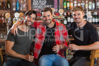 Portrait of smiling male friends holding beer bottles in bar