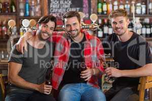 Portrait of smiling male friends holding beer bottles in bar