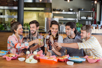Cheerful friends toasting beer while sitting in restaurant
