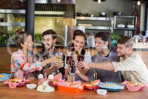 Cheerful friends toasting beer while sitting in restaurant