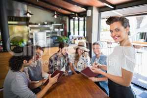 Smiling waitress standing by customers in restaurant