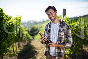 Portrait of young man holding wine bottle at vineyard