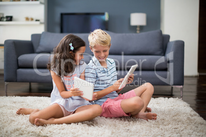 Siblings sitting on rug and using digital tablet in living room