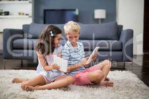 Siblings sitting on rug and using digital tablet in living room