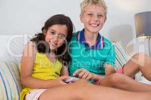 Portrait of smiling siblings using digital tablet on bed in bedroom