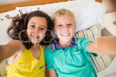 Smiling siblings taking selfie in bedroom