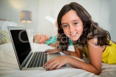 Portrait of smiling girl using laptop on bed in bedroom