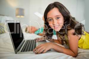 Portrait of smiling girl using laptop on bed in bedroom