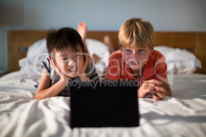 Smiling siblings looking at digital tablet on bed