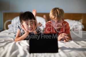 Smiling siblings looking at digital tablet on bed