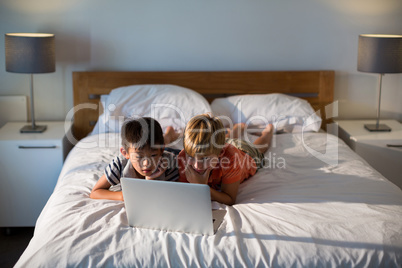 Siblings using laptop on bed