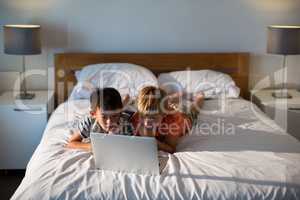 Siblings using laptop on bed